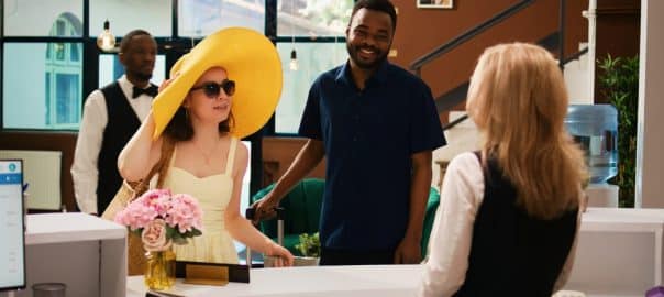 Receptionist welcoming tourists in lobby upon their arrival at tropical summer resort. Hotel guests travelling on honeymoon with room accommodation, check in at reception counter.