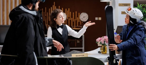 In hotel lobby, young couple interacts with helpful staff for check-in, reservations and assistance. Visitors in winter gear prepare for a ski holiday, capturing the excitement of a winter getaway.