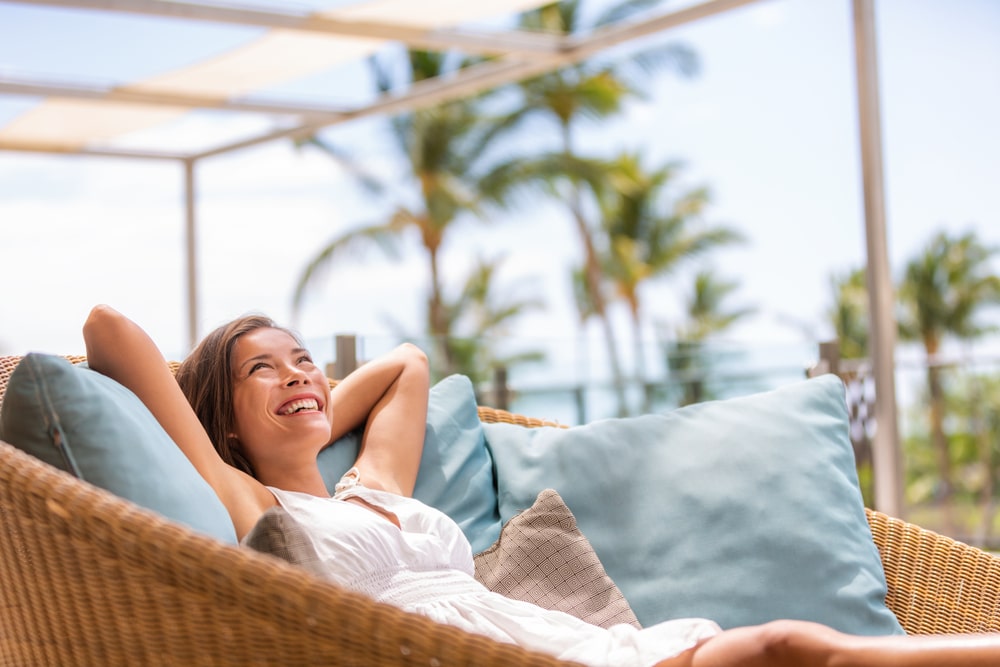 Hotel Room Relaxation Devices -- Woman relaxes on patio furniture with palm trees.