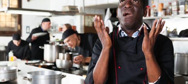 African American confident chef male in kitchen of restaurant.