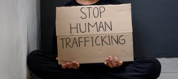 A little boy sitting crossed legs holding cardboard with text Stop Human Trafficking. Stop abusing violence.