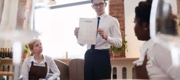 Young Asian manager working in modern restaurant showing new menu to waiting staff, selective focus shot.