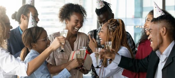 Overjoyed candid laughing african american female employee getting birthday surprise gift from friendly biracial colleagues, celebrating happy birthday, enjoying carefree hangout party in office.
