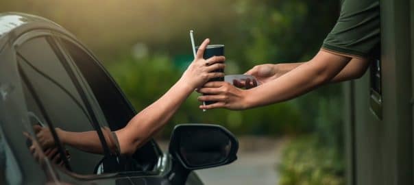 Hand Woman in car receiving coffee in drive thru fast food restaurant.