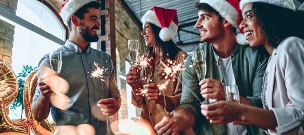 Multiracial young creative people are celebrating holiday in modern office. Group of young business people are drinking champagne with sparkling bengal light.