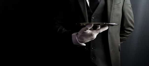 Portrait of Butler or Waiter in Dark Formal Suit and White Gloves Elegantly Holding Silver Serving Tray. Copy Space for Service Industry and Elite Hospitality.