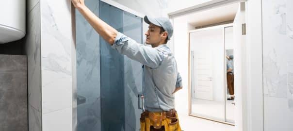 Workers are installing glass door of the shower enclosure.