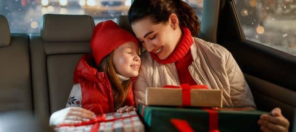 Woman and her child holding presents and delivering them on car to home. Holidays concept. Time of Christmas Eve.