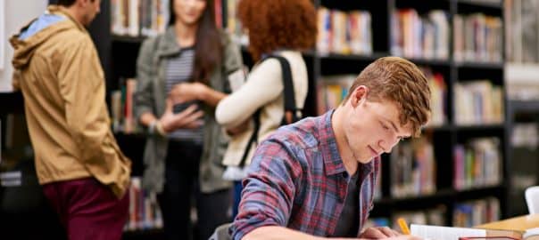 Student, writing and notebook in library for study, education and university quiz with pen on table. Man, books and knowledge on school campus for college, research and learning with scholarship.