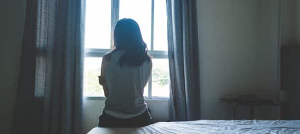 Woman sitting on bed in room with light from window abuse concept.