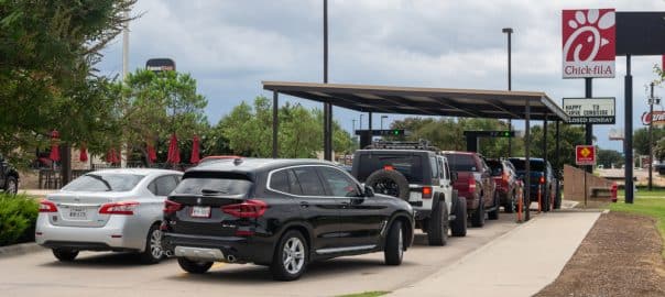 A Chick-fil-a restaurant is busy during the lunch rush, serving up fresh chicken sandwiches and french fries to hungry customers. The drive-thru line is quite long.