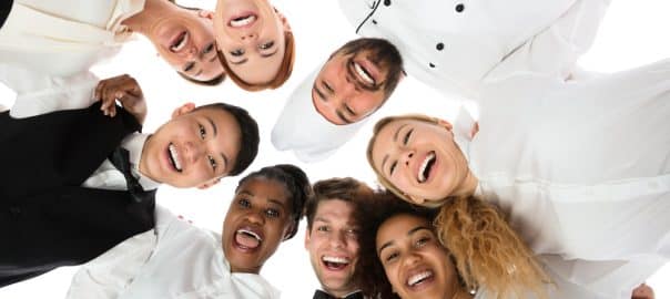 Low Angle View Of Happy Restaurant Staff Standing Against White Background.