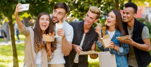 Girl is taking a picture of friends eating fast food in the park. Group photo, selfie for social media post.
