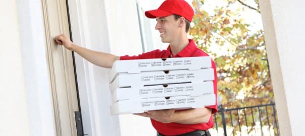 A handsome young pizza delivery man holding a pizza.