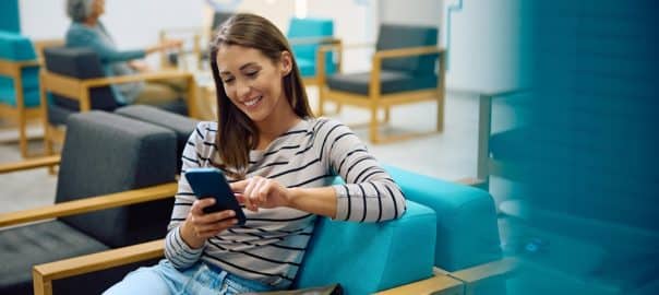 Happy woman using smart phone while waiting for doctor's appointment at medical clinic.