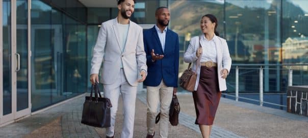 Business people, group and conversation in city on walk for commute to workplace with questions by buildings. Men, woman and employees with bag, outdoor and discussion for travel on metro sidewalk.