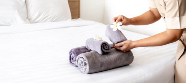 Hands of hotel maid putting plumeria flower and towels on the bed in the luxury hotel room ready for tourist travel.