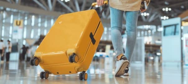 Female traveler passenger walking with a yellow suitcase at the modern Airport Terminal, Back view of woman on her way to flight boarding gate, Ready for travel or vacation journey.