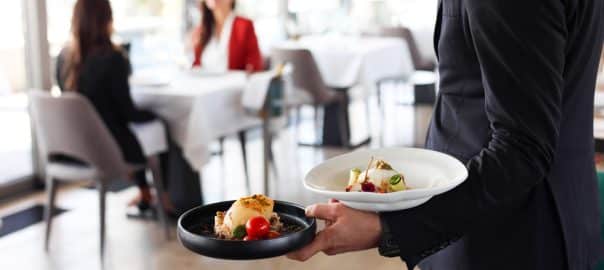 Waiter from a luxury restaurant carrying delicious dishes for two businesswomen on a business lunch.