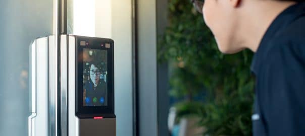 Authentication by facial recognition concept. Biometric admittance control device for security system. Asian man using face scanner to unlock glass door in office building.
