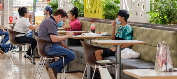 Father and son at a plantation mall food court eating lunch during the covid 19 coronavirus pandemic wearing face mask personal protective covering.