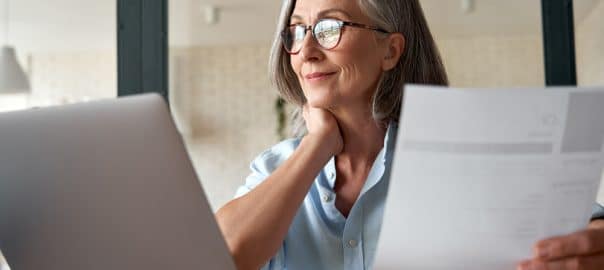 Smiling mature middle aged business woman using laptop working on computer sitting at desk. Happy old businesswoman hr holding cv interviewing distance applicant, senior seeker searching job online.
