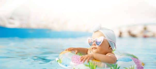 Cute funny toddler girl in colorful swimsuit and sunglasses relaxing on inflatable toy ring floating in pool have fun during summer vacation in tropical resort. Child having fun in swimming pool.