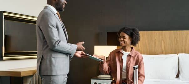 Portrait of smiling Black woman as guest putting in digital signature on tablet in hotel room copy space.