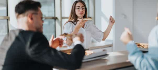 A group of business employees enjoying pizza during a casual lunch break in a modern office environment. They engage in conversation, fostering relationships and boosting morale.