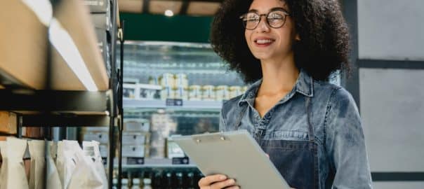 Young attractive african barista bartender waitress checking the quality of goods, doing inventory taking notes holding a folder clipboard in coffee shop cafeteria.