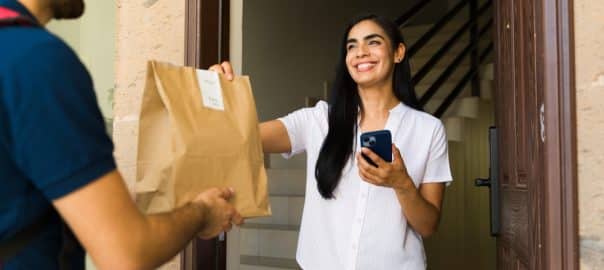Customer delighted to receive a food delivery at home from a delivery person using a smartphone app.