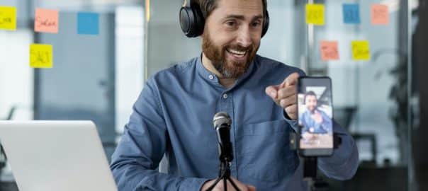 Man recording podcast in modern office setting with headphones, microphone, and smartphone. Professional setup for audio and video content creation. Engaging in remote communication, social media.
