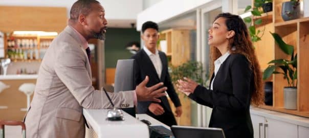 Businessman, woman and angry at cafe with stress, argument and complaint for bad service at hotel. People, dispute and frustrated with conflict, fight and talking by counter with question for staff.