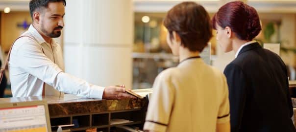 Serious man showing booking information on smartphone to manager at hotel reception.