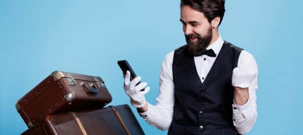 Staff member of excellent hotel is messaging and browsing internet, reading positive information over studio background. While using telephone, bellhop is acting lively and skilled.