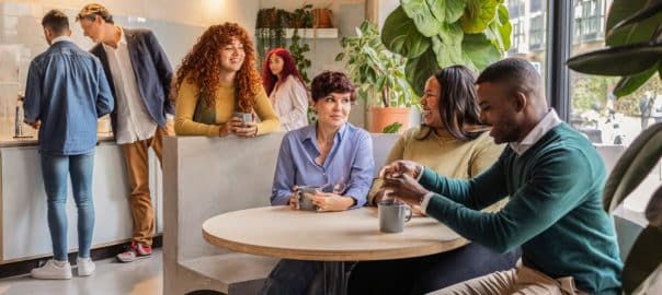 Multi ethnic colleagues enjoying a coffee break, engaging in lively conversation and building teamwork in a modern office setting, creating a relaxed atmosphere for connection and collaboration.