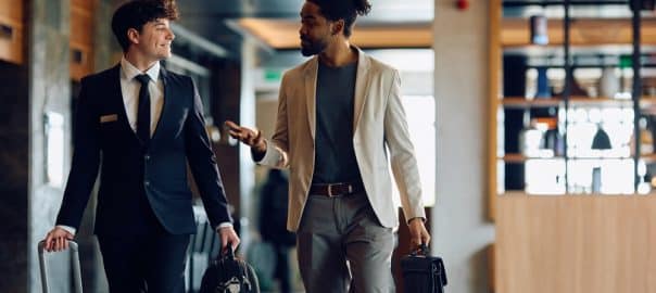 Happy hotel attendant talking to African American guest while carrying his luggage through the lobby. Copy space.