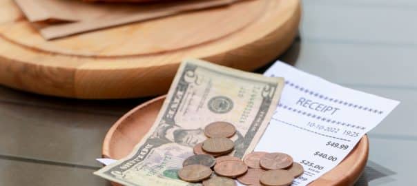 Tips, receipt and croissant on wooden table, closeup.