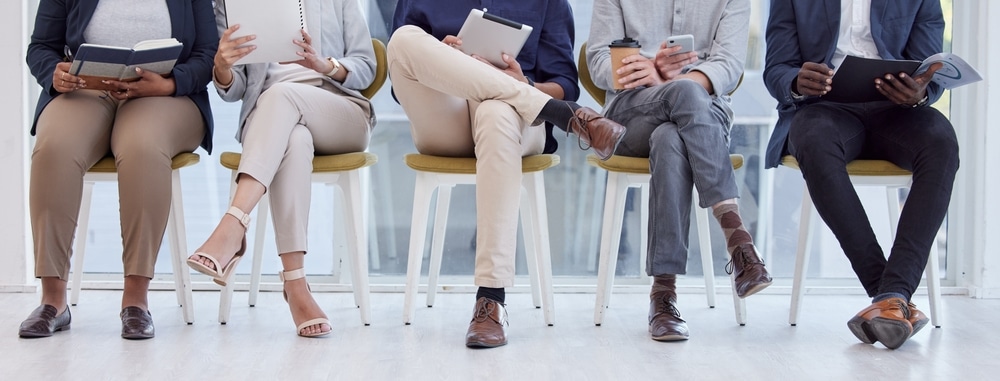 Recruitment, people and queue in waiting room for job interview, hiring or legs on chair in line. Group, lobby or scroll phone or tech in human resource office with resume, info and opportunity.