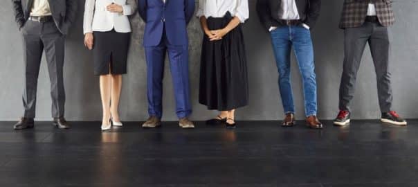Legs of business people stand against a concrete wall for a corporate team portrait highlighting leadership and teamwork. Six professionals standing in a row in office. Teamwork concept.