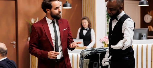 Bellboy taking guest to his hotel room, providing excellent luxury service for businessman with luggage. Bellhop carrying suitcase for traveller, formal client on business trip.
