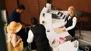 People,Arriving,At,Hotel,Front,Desk,,Preparing,To,Do,Check People arriving at hotel front desk, preparing to do check in at reception counter and see room reservation. Guests on honeymoon during summertime talking to concierge in lobby. Handheld shot.
