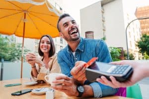 Happy,Young,Adult,Man,Paying,The,Bill,With,A,Contactless Happy young adult man paying the bill with a contactless credit card on a restaurant, bar or coffee shop. Handsome male smiling holding a creditcard and giving a payment transaction to the cashier